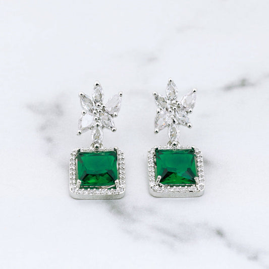 Pair of earrings with diamonds and green gemstones on a marble background