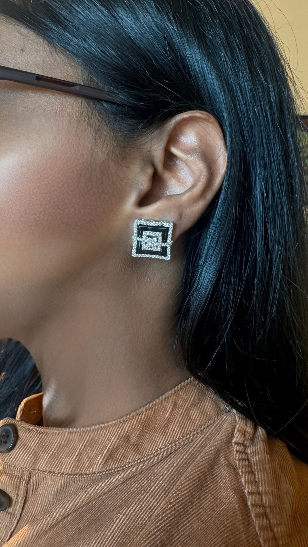 Person wearing a square earring with a logo, close-up of the ear.