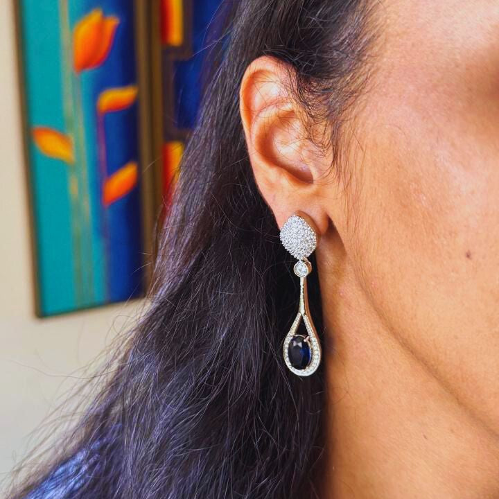 Close-up of a person wearing silver earrings with a colorful abstract painting in the background.
