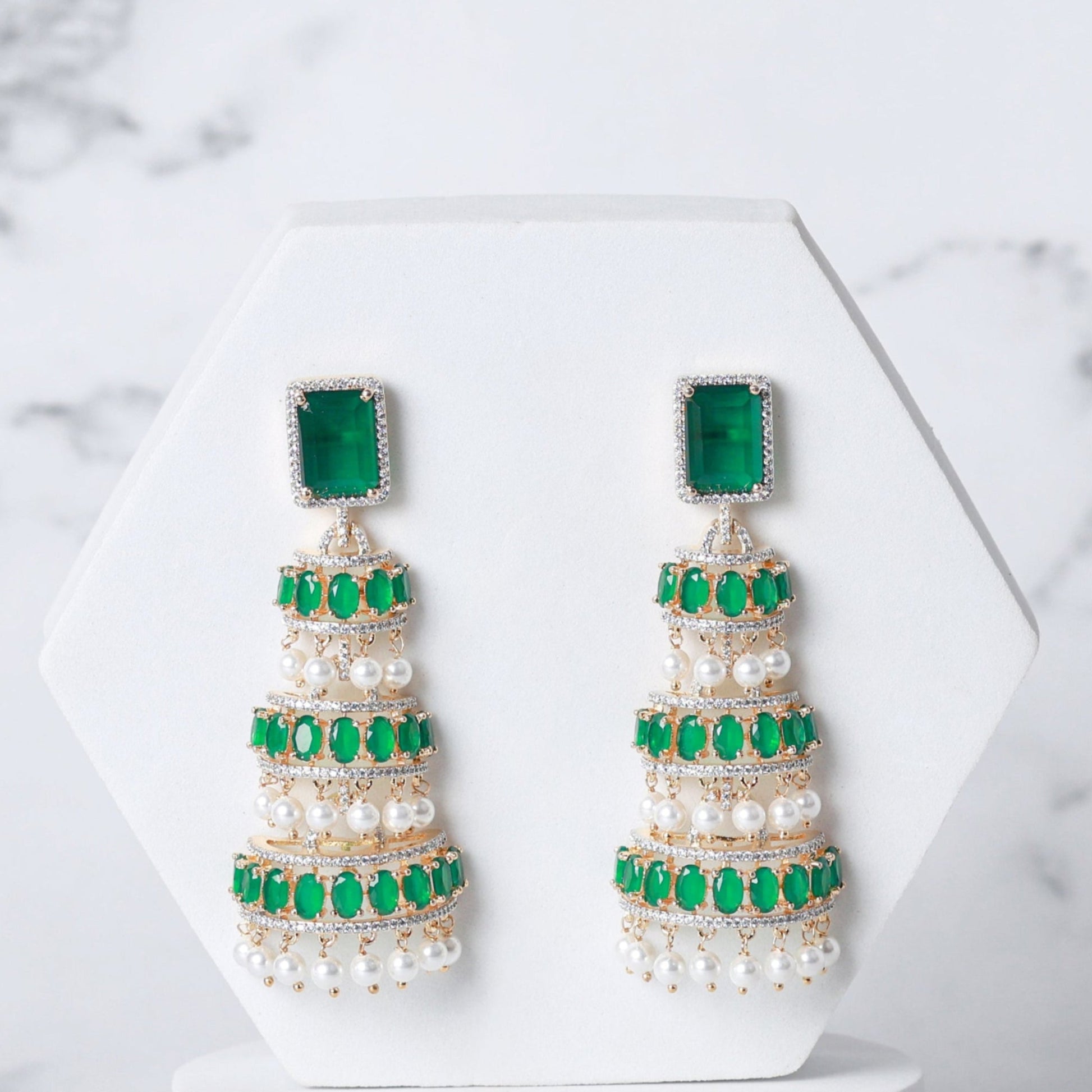 Pair of pearl earrings with green accents on a white marble background