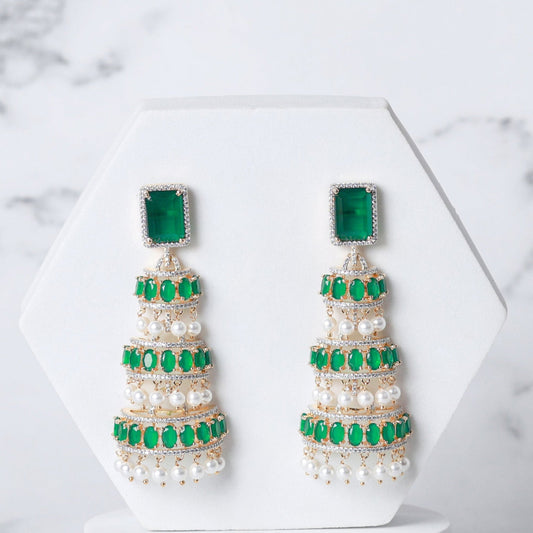 Pair of pearl earrings with green accents on a white marble background
