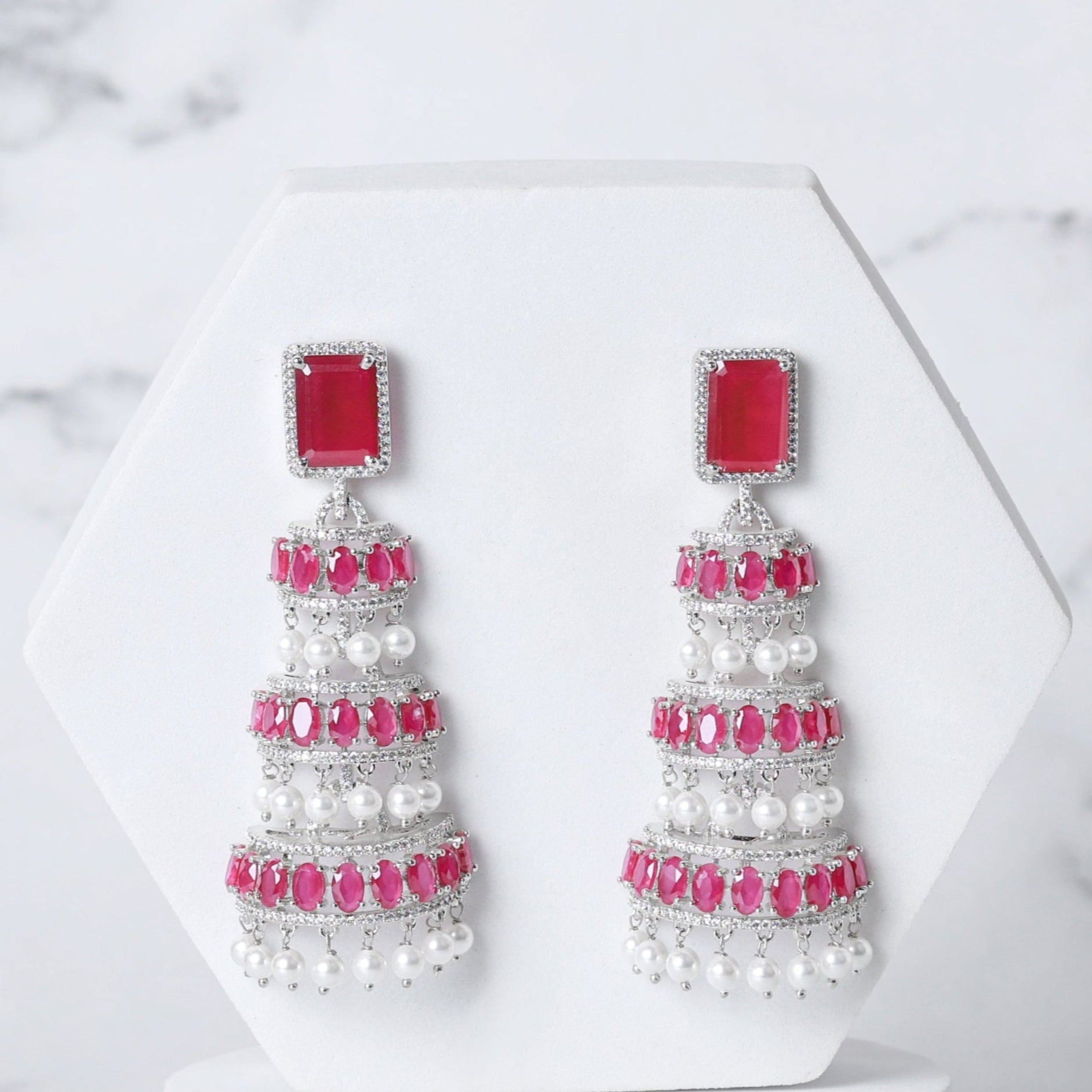 Pair of earrings with red and white stones on a marble background