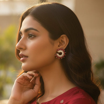 Woman in a red traditional outfit with floral earrings, standing outdoors.